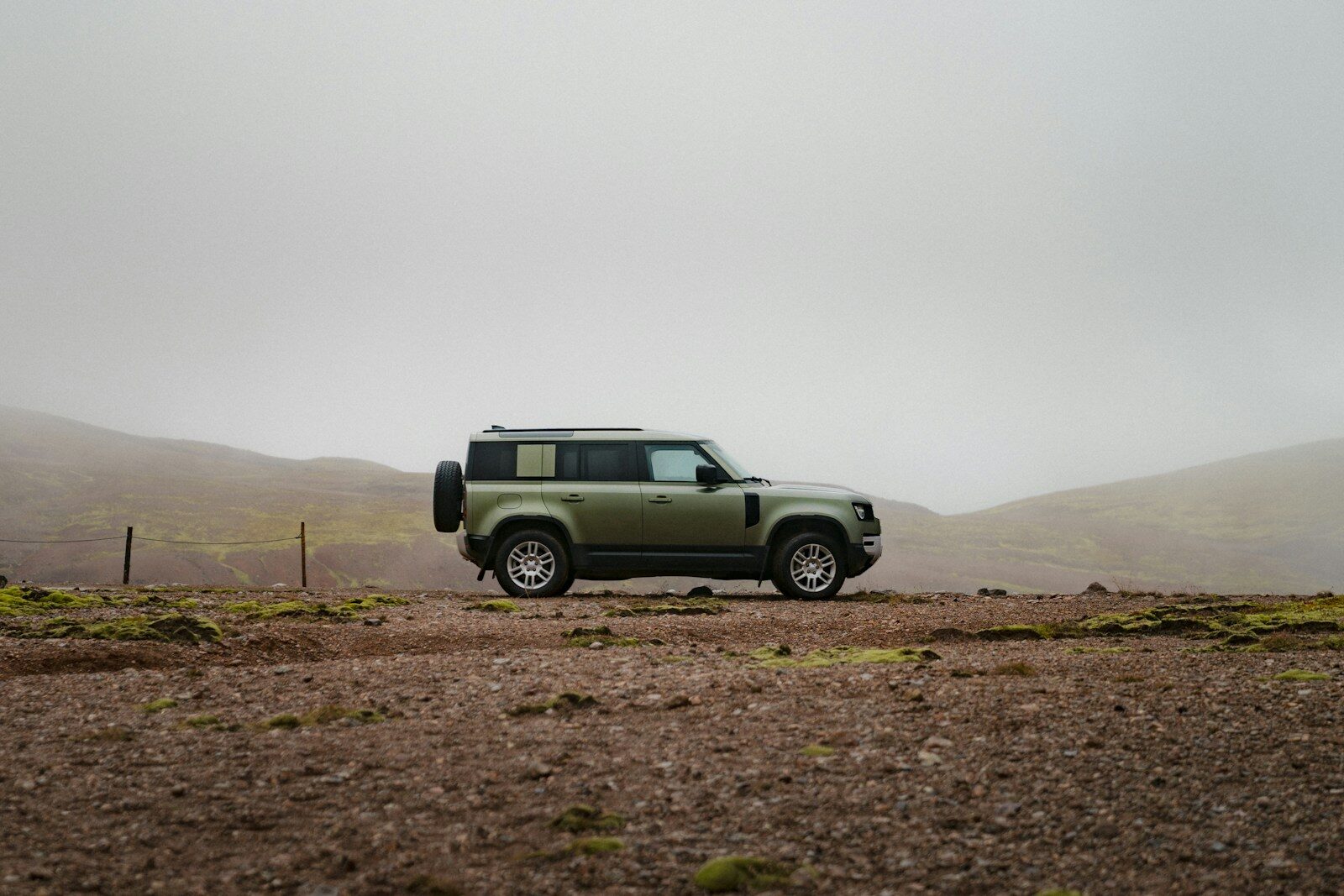 A green off-road vehicle parked on a rocky landscape under a foggy sky